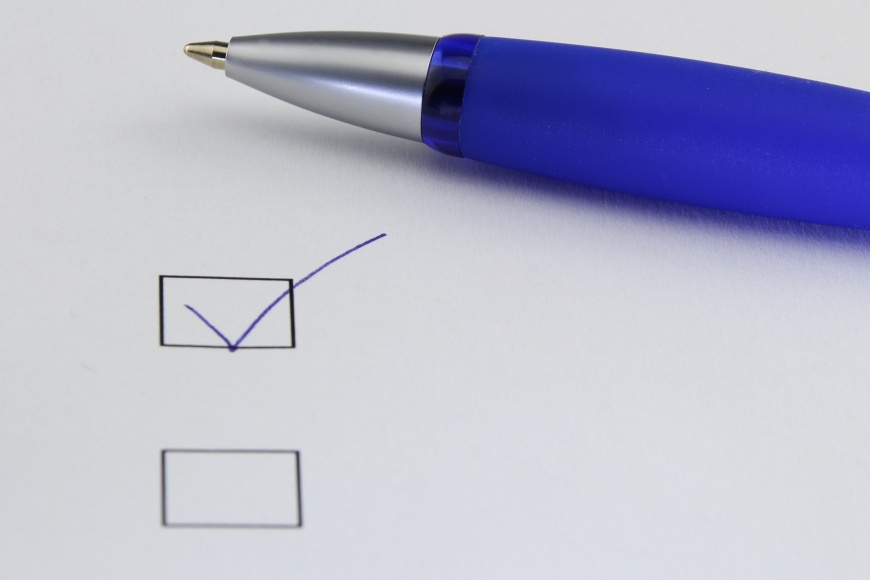 Papierblatt auf dem ein Kugelschrieber und eine Checkbox abgehakt ist.