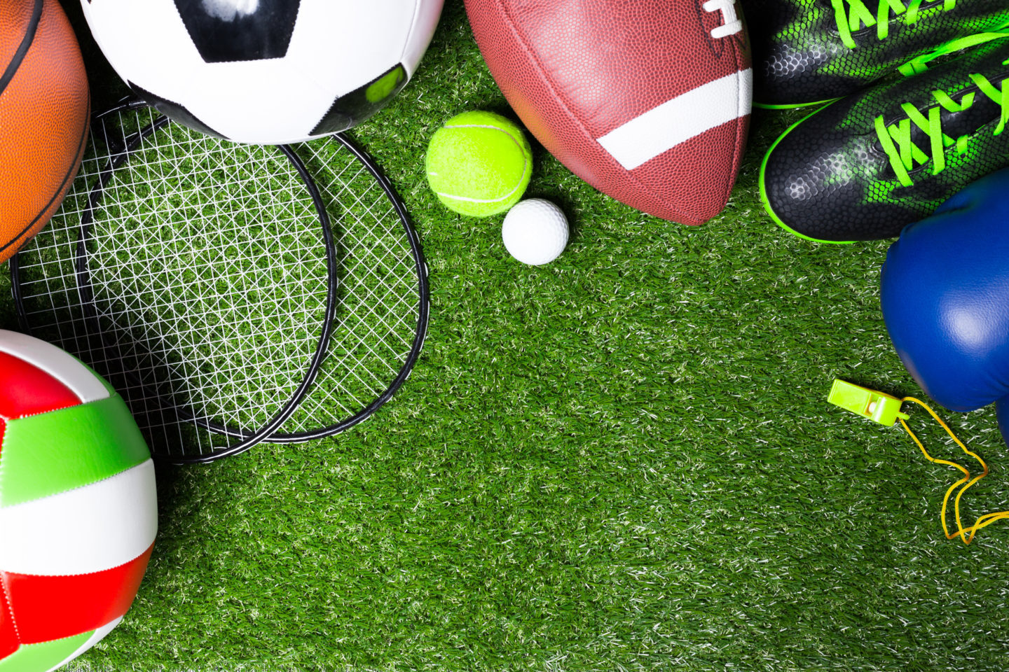Eine Wiese auf der ein Volleyball, ein Basketball,, Badmintonschläger, ein Fußball, ein Tennisball, ein Golfball, ein Football, Fußballschuhe, ein Boxhandschuhe und eine Trillerpfeiffe liegen