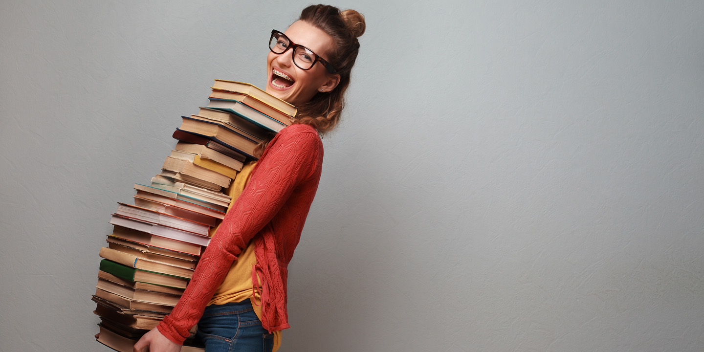 Junges Mädchen fröhlich mit ganz vielen Büchern am Tragen