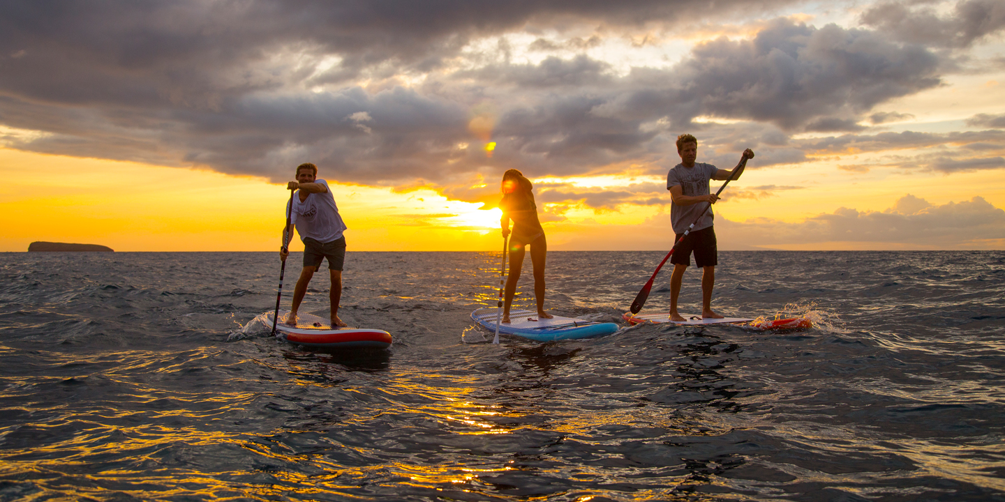 3 Personen stehen am SUP bei Sonnenuntergang am Wasser