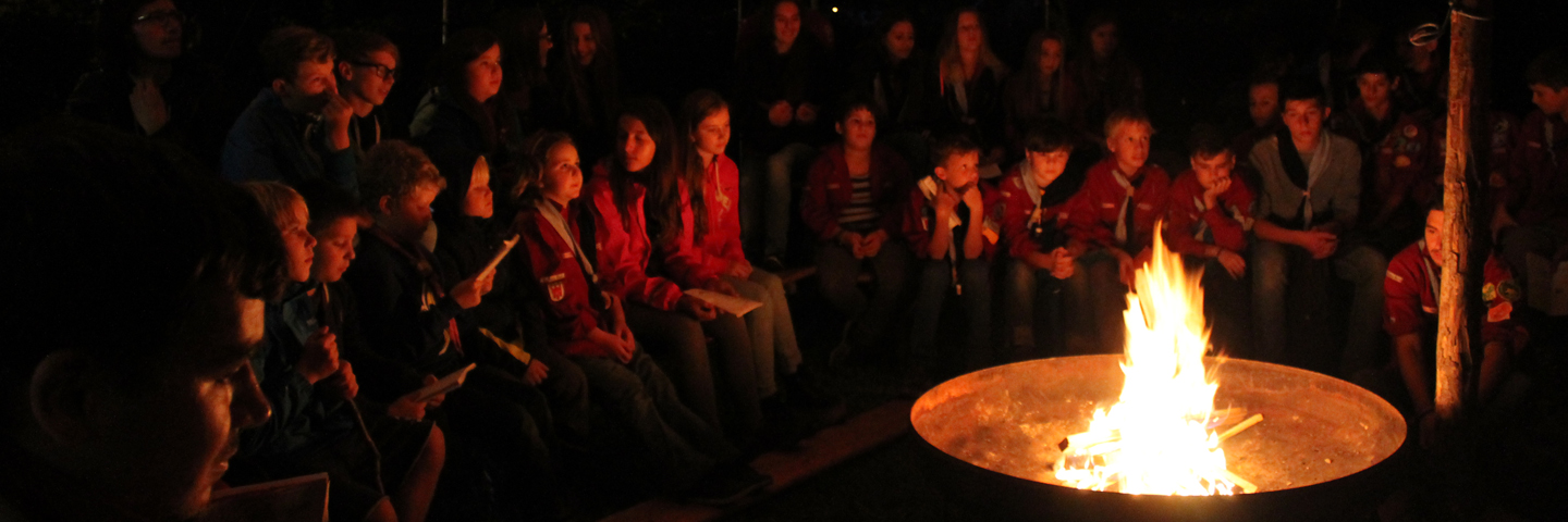 Pfadfinderinnen und Pfadfinder sitzen rund um ein Feuer.