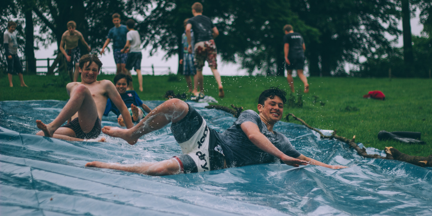 Junge Burschen runtschen eine Wasserplane runter.