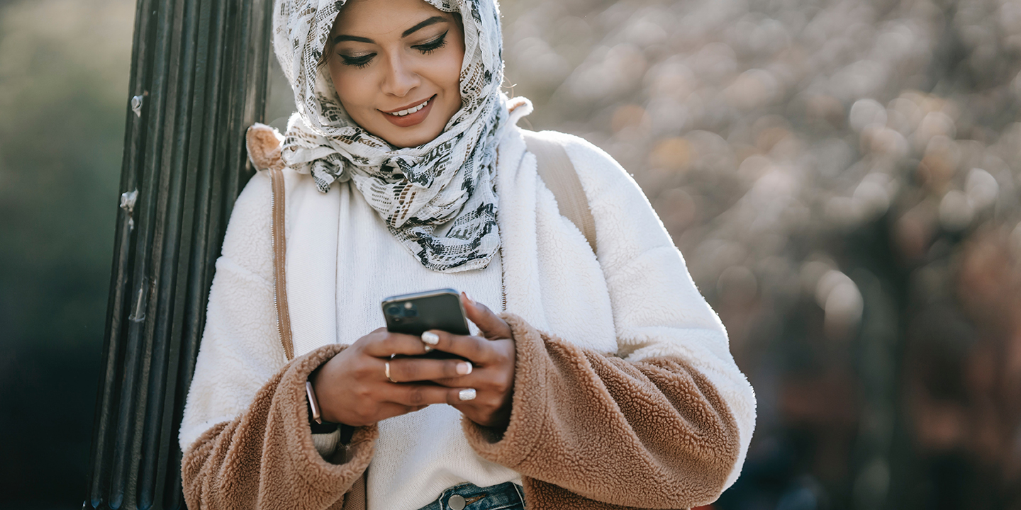 Eine junge Frau schaut in ihr Smartphone und lächelt.