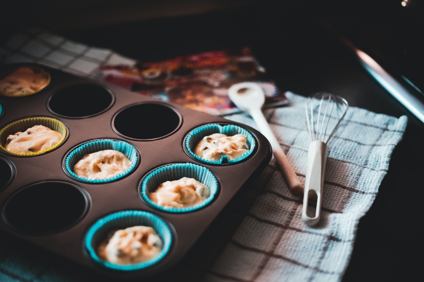 Das Bild zeigt ein Muffinblech und Backutensilien.