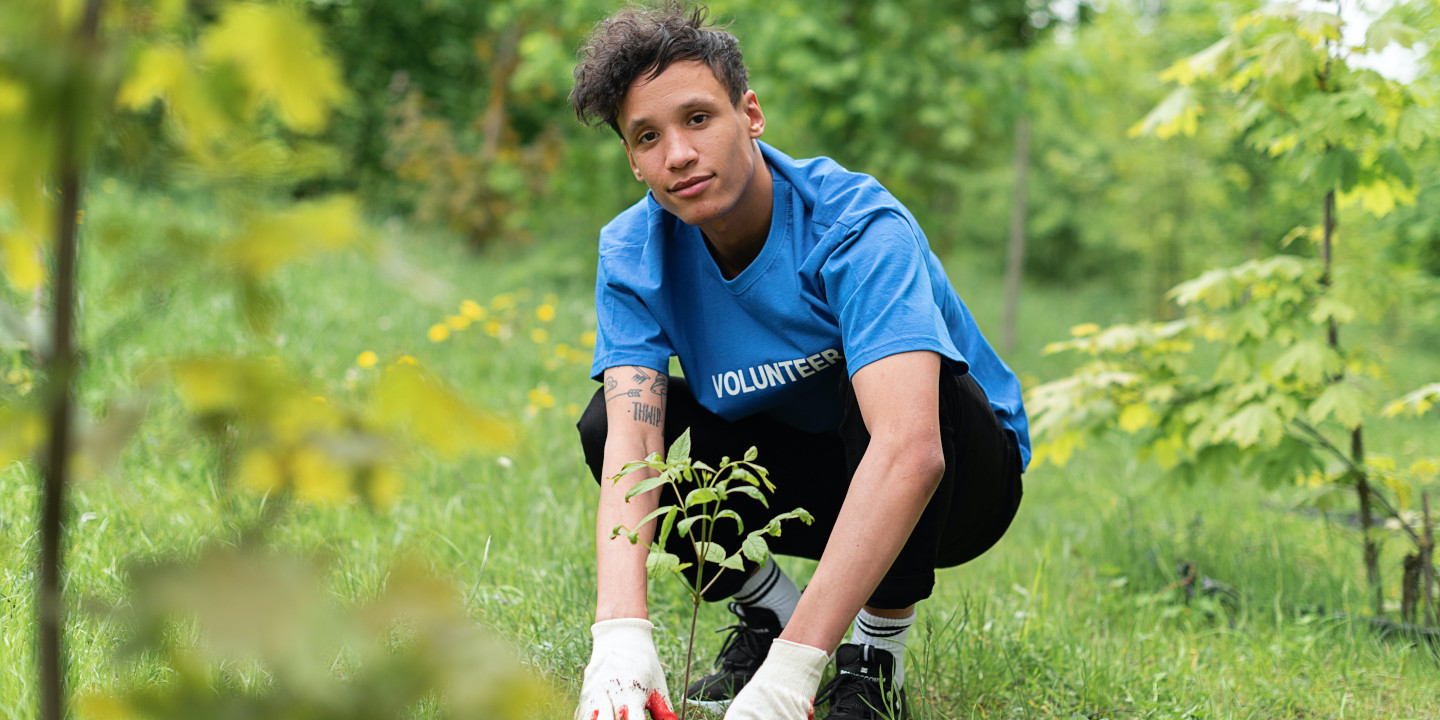 Jguendlicher in einem blauen Shirt pflanzt einen Baum