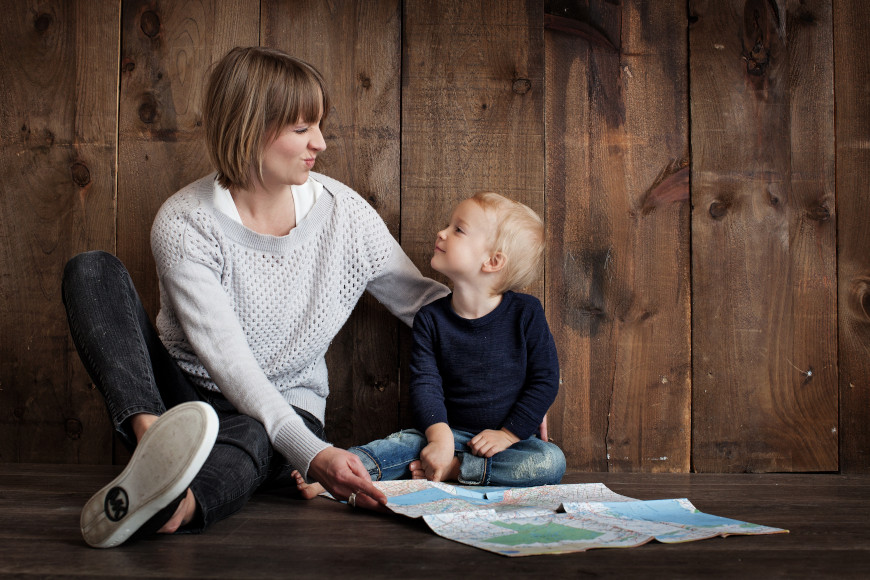 Eine junge Frau und ein Bayb sitzen nebeneinander und lächeln sich an.