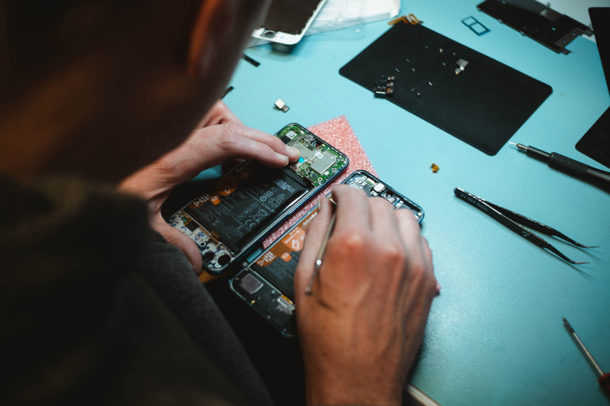 Eine Perosn Reparatiert ein Smartphone und sitzt vor einem Handy ohne Hülle.