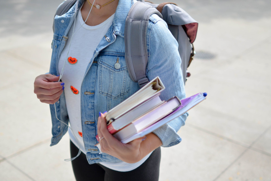 Person mit Rucksack und Büchern und einer Mappe in der Hand.