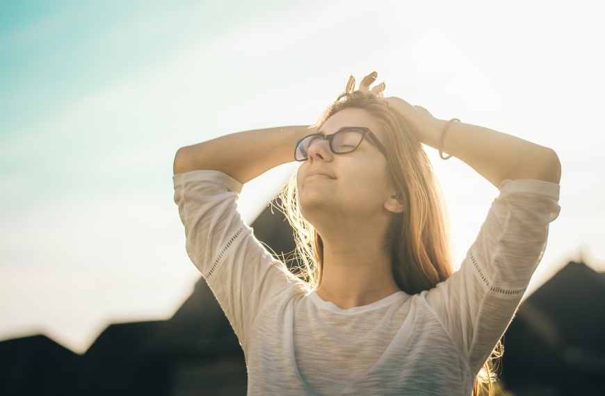 Mädchen, das mit geschlossenen Augen und Händen über dem Kopf die Sonne genießt