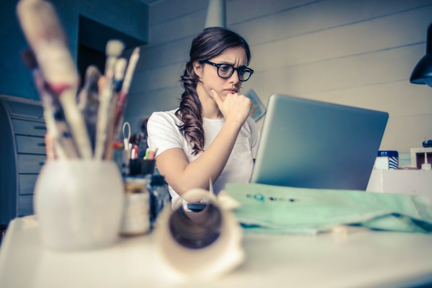 Eine junge Frau sitzt nachdenklich vor einem Laptop.