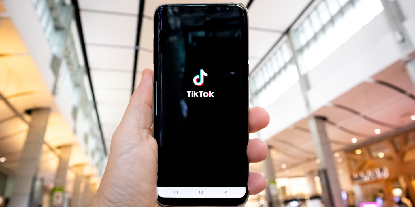 eine Perosn hält ein Smartphone in der Hand auf dem man den Startscreen von TikTok sieht