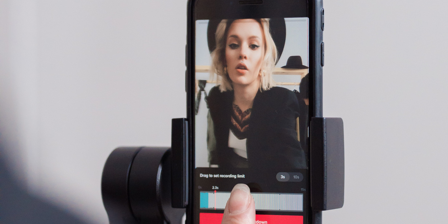 Eine junge Frau macht ein TikTok-Video von sich und man sieht sie im Smartphone