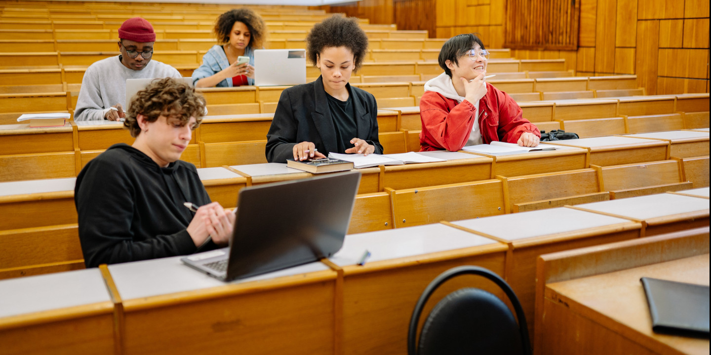 Eine Gruppe von jungen Erwachsenen sitzt in eine Hörsaal und schauen ihn ihre Computer oder machen Notizen auf Papier.
