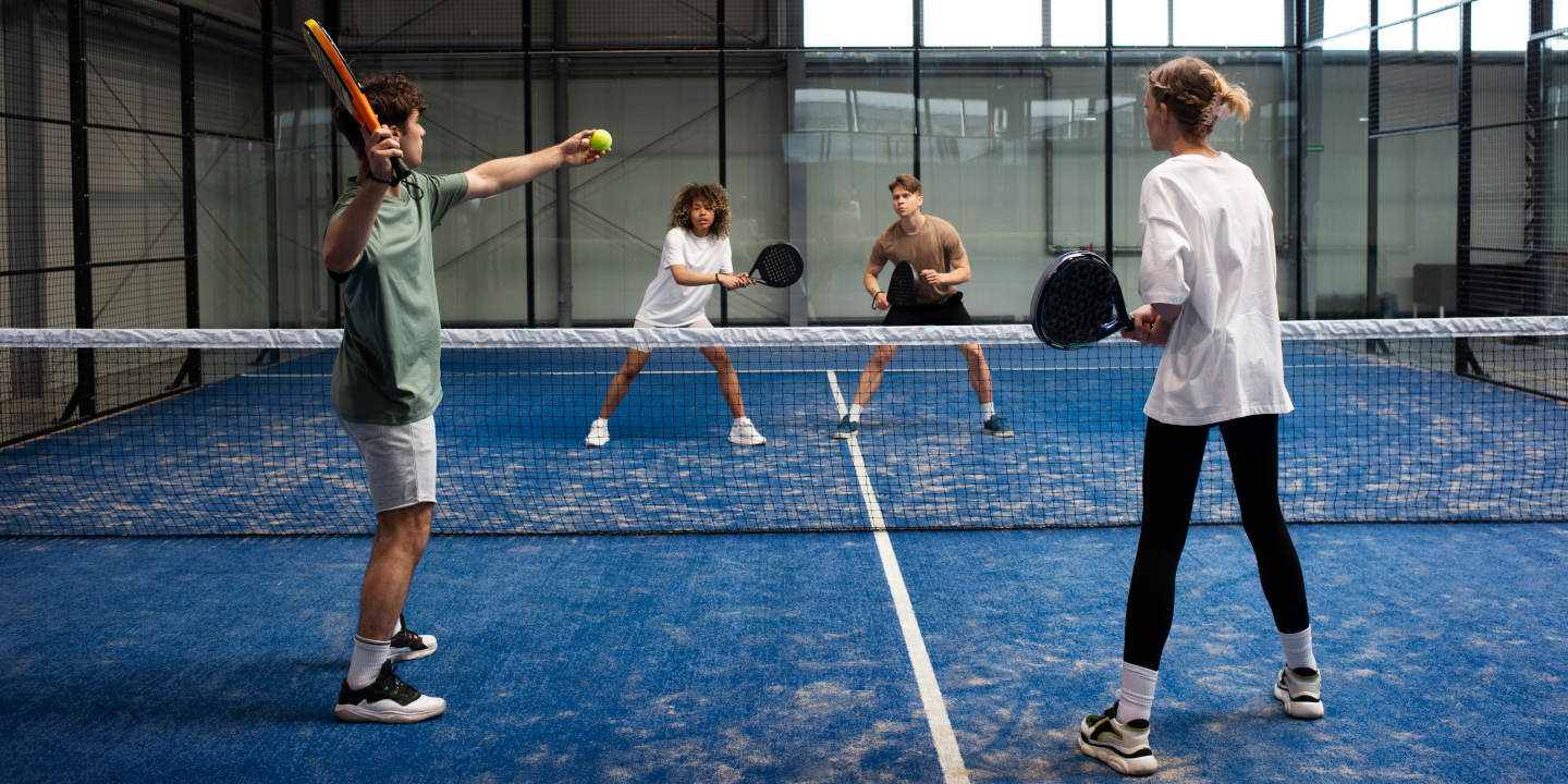 Vier Jugendliche spielen gemeinsam Paddle-Tennis in einer Halle.
