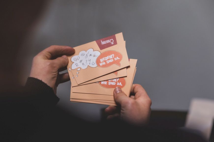 Eine person hält eine Postkarte vom Verein Amazone in der Hand auf der Steht "Reden? Wir sind da."