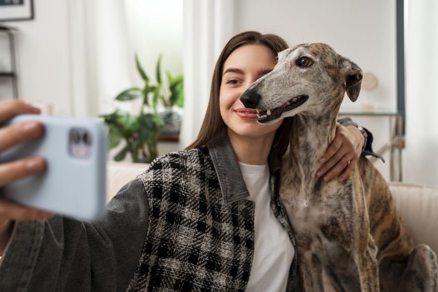 eine Jugendliche sitzt auf einer Couch und macht ein Selfie mit ihrem Hund.